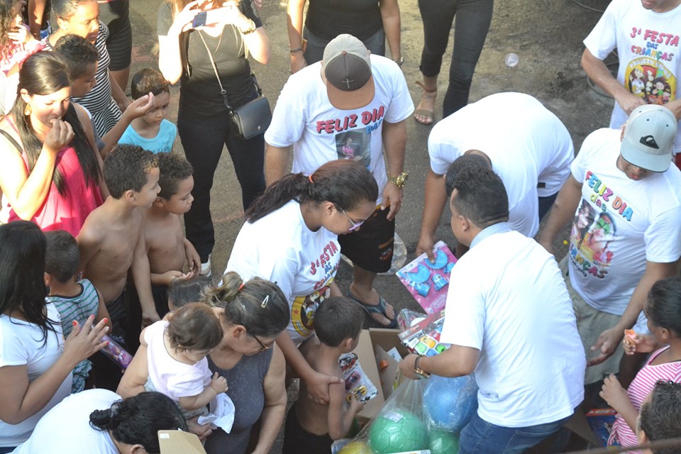 Algumas crianças, acompanhadas por adultos, escolhem os brinquedos. O subprefeito do Itaim Paulista distribui alguns dos presentes no local. 